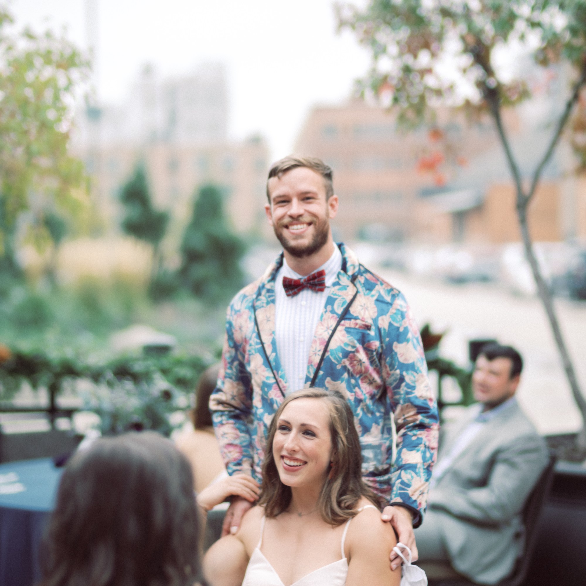 Dustin smiles at the camera with his hands on Haley's shoulders, who is looking away.